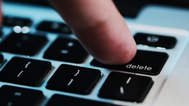 Finger of the computer user, he presses the delete button on the computer keyboard	