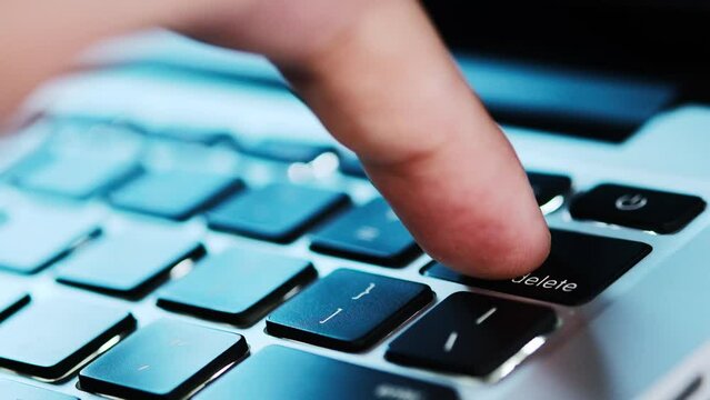 Finger of the computer user, he presses the delete button on the computer keyboard	