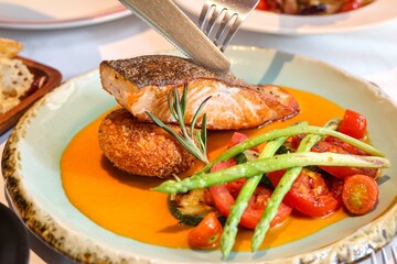 Fried salmon fillet with fried potatoes, lime and vegetable salad served on black plate on wooden table