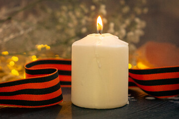Burning candle and St. George's ribbon against a background of burning lights