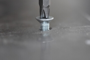 A screwdriver screws a bolt into a metal sheet