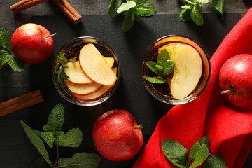 Glasses with apple cider, mint leaves and red apples on dark wooden background, top view