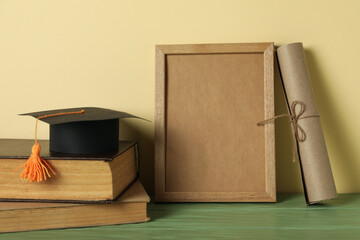 Frame and graduate hat with books on table.