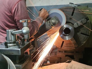 An engineering worker cutting stainles Steel bar with hand cutting grinder . mounted on lathe...