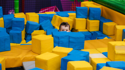 A boy child is playing in a game entertainment nursery. He plays with soft large cubes. Active pastime in the amusement park.