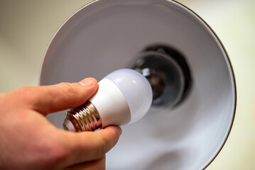 White LED light bulb in male`s hand, holding it near the the lamp with incandescent bulb. Changing the house lightning, concept of energy-efficiency
