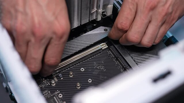 Close-up hands of unrecognizable man computer repair technician male removing cover on motherboard to install new SSD disk. Stages of assembling electronic equipment for work. Shooting in slow motion.