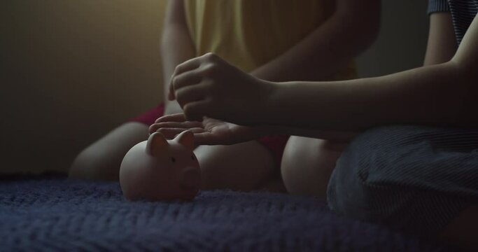Children throw coins into a pink pig piggy bank. Coins in a piggy bank symbol of banking security. Financial savings are kept in bank. Concept of children preparing for business and financial security