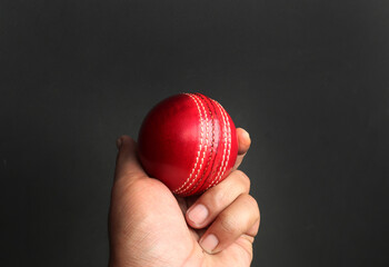 red cricket leather ball in player's hand on the dark background