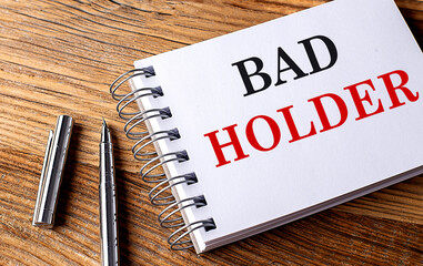 BAD HOLDER text on notebook with pen on the wooden background 