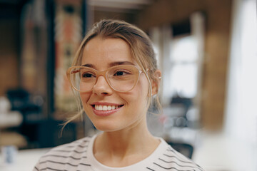 Portrait of smiling female freelancer in eyeglasses standing on coworking background and looks away