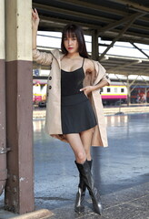 Beautiful Asian woman wears trenchcoat over short black dress, train in the background