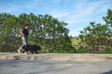 Young woman is running with a dog, a cute black cocker spaniel on a leash in the summer time, sunny...