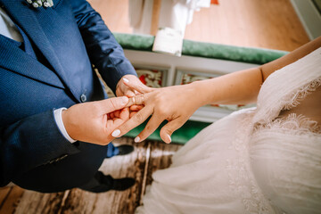 Fototapeta premium Valmiera, Latvia - August 25, 2023 - Close-up of a bride and groom exchanging wedding rings, focusing on their hands against a background of the bride's lace dress...
