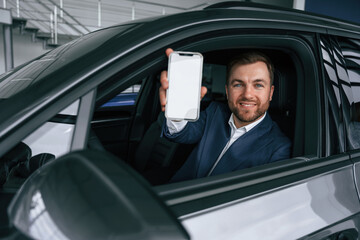 Smartphone with copy space on display. Businessman is in the brand new car
