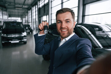 Making a selfie, with keys for new automobile. A businessman is in a car dealership