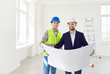 Male builder and engineer happy holding project paper plan for apartment repair, renovation,...