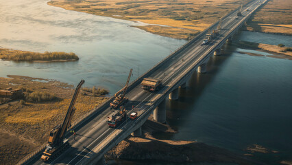 Aerial view of cranes and crew constructing bridge spanning river, Highway infrastructure transportation logistics construction project