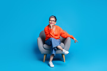 Full body photo of lovely senior lady sit armchair look minded empty space dressed stylish orange garment isolated on blue color background
