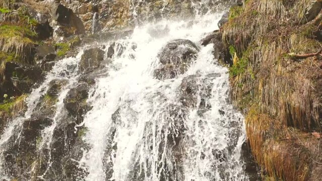 ripresa in tempo reale ed in primo piano di una piccola cascata in un ambiente naturale di montagna, illuminato dal sole, di giorno, in primavera