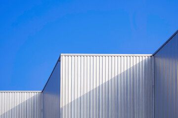 Aluminium corrugated steel wall of geometric industrial building against blue clear sky background...