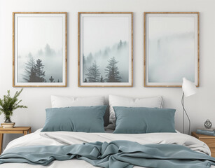 Minimalist bedroom with three wooden frames above the bed, nature landscape posters in each frame of a misty forest. Pastel blue and white bed sheets blue and white pillows, grey wall.