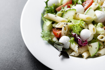 Pasta salad with vegetables and mozzarella cheese on black background. Close up