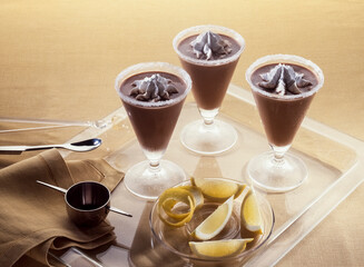 Three glasses of chocolate mousse with cream on glass tray