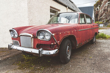 Old maroon car abandoned next to a house.