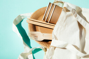 A paper utensils, plates and wooden cutlery on a textile bag on a blue background. Eco friendly...