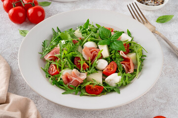 Fresh summer salad with arugula, melon, prosciutto and mozzarella cheese on concrete background, Healthy food. Top view.