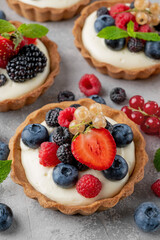 Tartlets with custard vanilla cream with fresh berries and mint on a gray concrete background. Summer dessert.