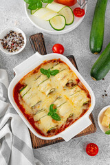 Baked zucchini rolls with ground meat, tomato sauce and cheese in a white baking dish on a gray concrete background. Selective focus, top view.