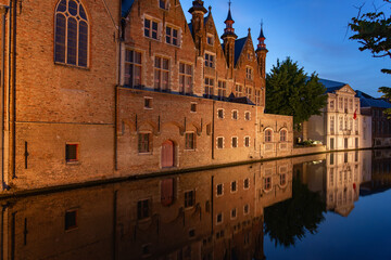 Historic buildings reflected on the canal in the old town of the beautiful city of Bruges in Belgium with the Meestrat bridge in the background at night.