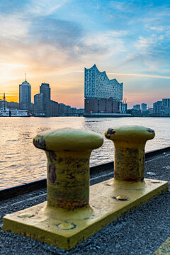Blick auf die Elbphilharmonie morgens im Sonnenaufgang von der Elbinsel Steinwerder aus, gelbe Festmachpoller im Vordergrund, horizontal