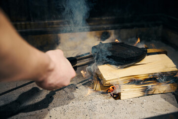 Person hand holding pancake maker over woods in burning open stove