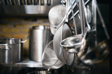 Focus on foreground of hanging cooking utensils and blurred table with saucepans