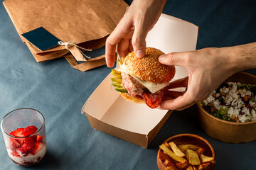 Hands Grabbing Burger from EcoFriendly Box: Sustainable Delivery Meal Packaging - Unpacking Ready...