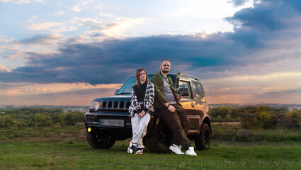 Travelers Couple. Road Trip, Man and Woman on Journey Near Their SUV off road Car Over Beautiful Landscape. Sunset clouds. Copy space. - Powered by Adobe