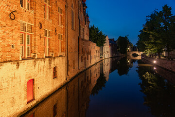 Historic buildings reflected on the canal in the old town of the beautiful city of Bruges in Belgium with the Meestrat bridge in the background at night.