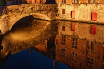 Blinde-Ezelbrug bridge and the historic buildings reflected on the canal in the old town of the beautiful city of Bruges in Belgium at night.