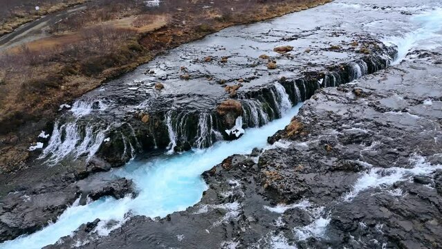 Aerial shot of the striking Bruarfoss waterfall with vibrant blue waters in Iceland, barren landscape