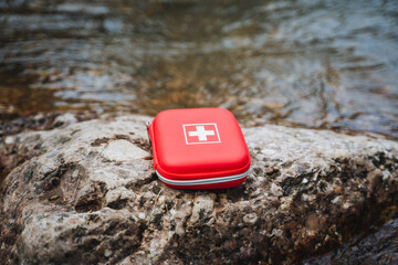 Naklejka premium A red first aid kit rests on a rock beside the river