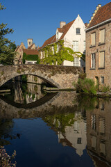 Fototapeta na wymiar Peerden bridge and historic buildings reflected on the canal in the old town of the beautiful city of Bruges in Belgium in a sunny day.
