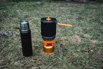 Thermos and pot placed on grass near stove fueled by gas