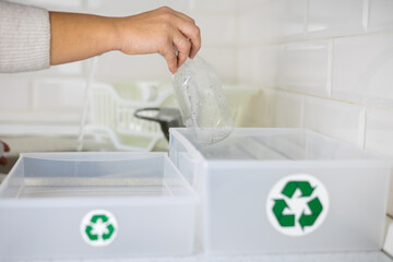 Against the background of boxes with a recycling sign, a woman washes plastic bottles. A woman...