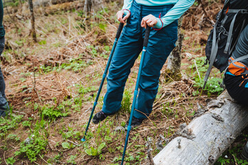 Woman in electric blue trousers standing on log in forest with hiking poles