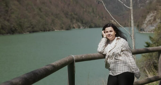 Woman Posing On The Fence With Mountains And Lake In The Background. - medium shot