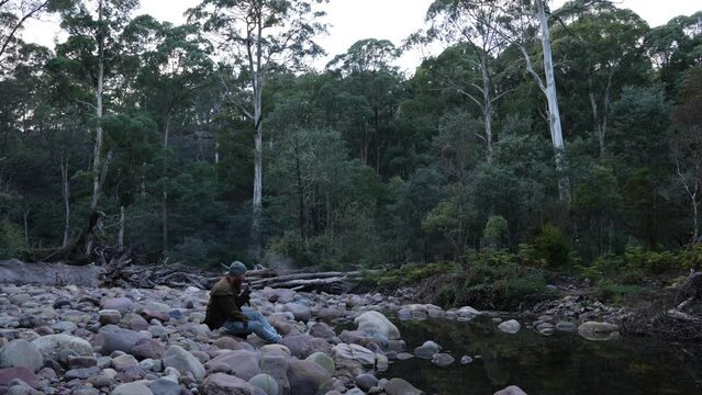 A bushman smoking a pipe by a river in the Australian bush.