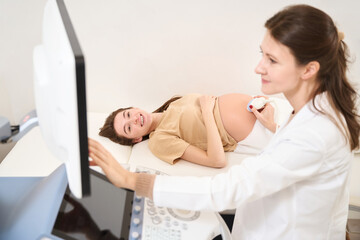 Gynecologist doing ultrasound scanning of pregnant belly of young european woman